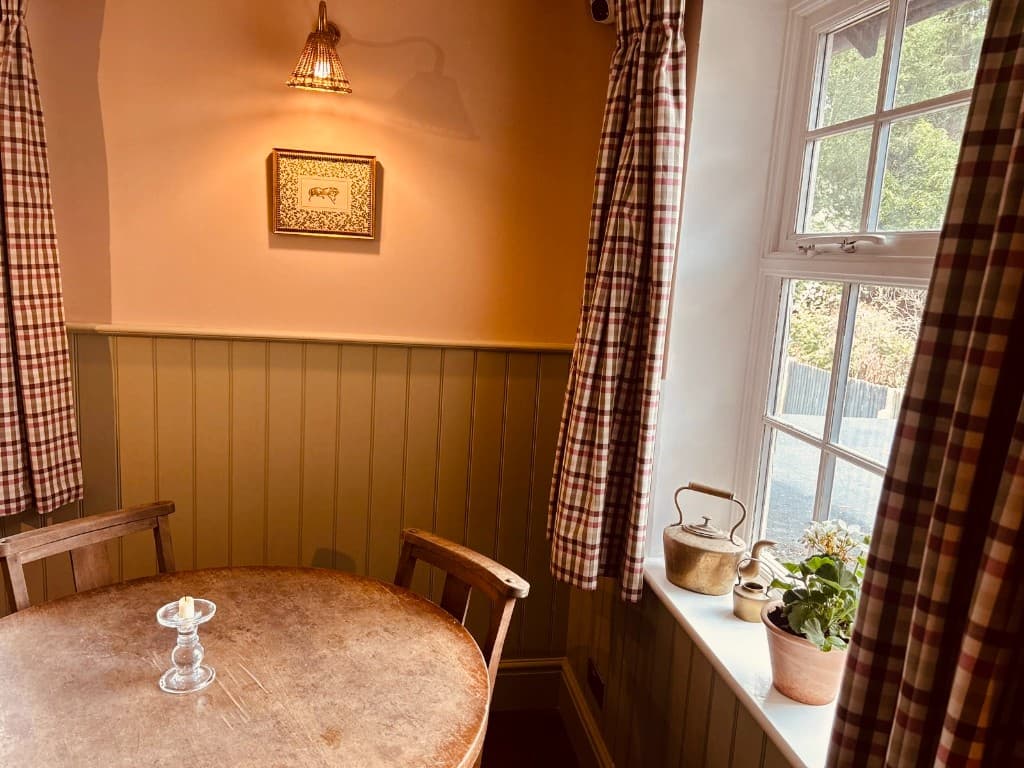 A window dining nook with check curtains and sage panelling at The Eight Bells