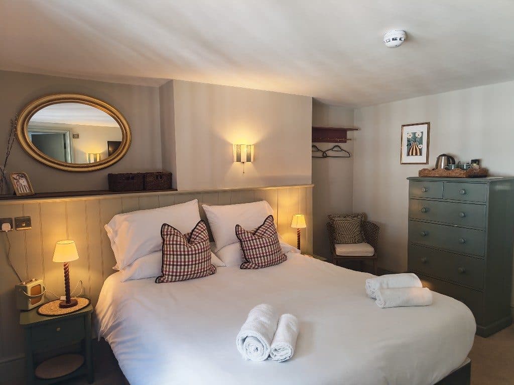 Room 2 at The Eight Bells — king bed with plaid cushions, gold oval mirror and sage panelling